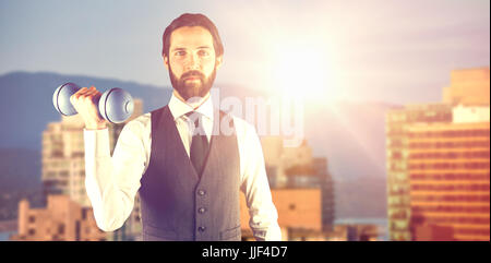 Portrait of businessman holding dumbbell contre les bâtiments en ville contre le ciel bleu Banque D'Images