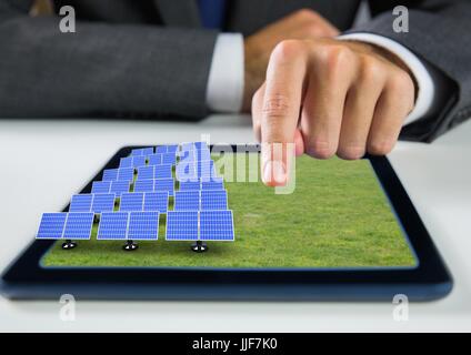 Digital composite de panneaux solaires sur l'herbe sur tablette avec businessman hand Banque D'Images