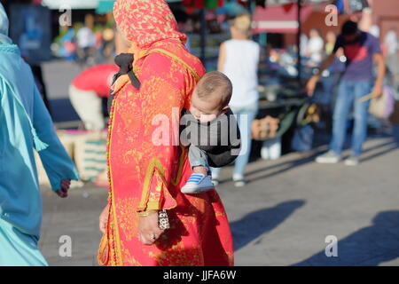 Morrocan dame portant son bébé, les doigts dans un chiffon, Marrakech, Maroc, Banque D'Images