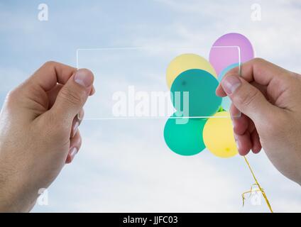 Digital composite des mains avec dispositif de verre contre ciel ensoleillé avec des ballons Banque D'Images