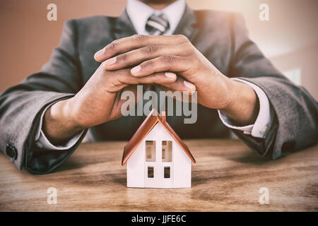 Modèle de maison d'affaires défendant avec les mains sur la table contre cette chambre lumineuse mur au milieu Banque D'Images