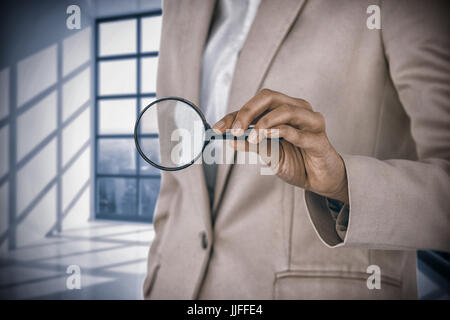 Mid section of businesswoman holding magnifying glass contre chambre avec grande fenêtre montrant city Banque D'Images