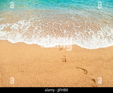 Empreintes de pas sur le sable humide et l'eau turquoise de la mer méditerranée avec soft mousse blanche aux beaux jours d'été en Espagne Banque D'Images