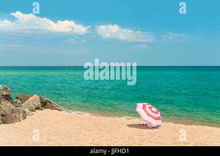 Stripy parasol coloré sur la plage de sable vide avec de gros rochers et l'eau turquoise de la mer Méditerranée, Santa Susanna, Catalogne, Spai Banque D'Images