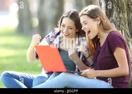 Adolescents excités de recevoir de bonnes nouvelles en ligne assis sur l'herbe dans un parc Banque D'Images