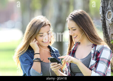 Deux amis happy teen partage de musique d'écoute et écouteurs smartphone dans un parc Banque D'Images