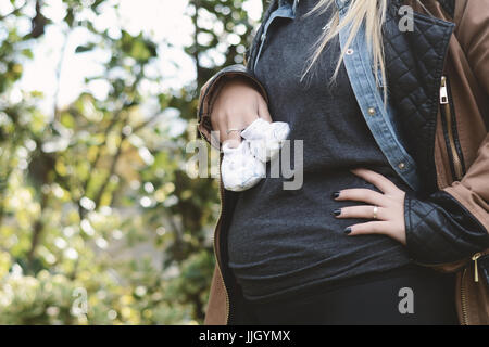 Portrait of beautiful young pregnant woman holding baby booties sur son abdomen. À l'extérieur. Banque D'Images