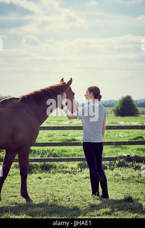 Une jeune femme debout avec son cheval dans un enclos. Banque D'Images