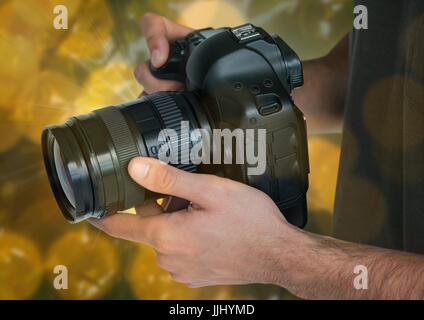 Appareil photo de photographe les mains. Arrière-plan flou vert et jaune et se chevauchent. Banque D'Images