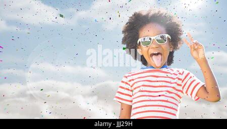 Garçon dans les lunettes faisant la paix signer contre ciel avec flare et confettis Banque D'Images