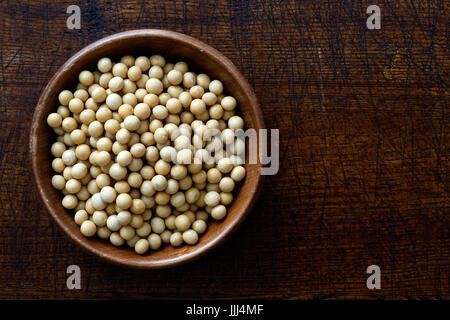 Sécher les graines de soja dans un bol en bois isolé sur bois marron foncé à partir de ci-dessus. Banque D'Images