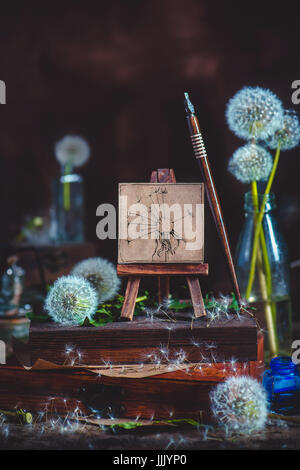 Encore l'été avec la vie, blowballs un peu le pissenlit sur un chevalet de peinture, encre et plume, pile de caisses en bois sur un fond de bois foncé Banque D'Images