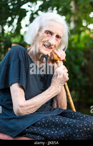 Cheerful senior femme assise avec une canne Banque D'Images