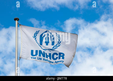 Drapeau de l'Organisation des Nations Unies pour les réfugiés (HCR) dans le vent au siège du HCR contre un ciel bleu avec des nuages. Banque D'Images