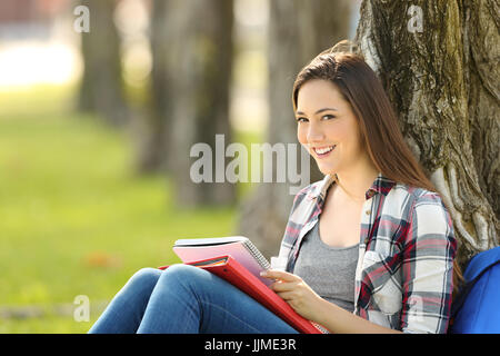 Satisfait student posing looking at you assis sur l'herbe dans un parc Banque D'Images