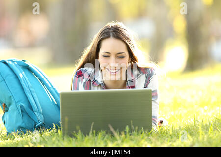 Vue de face d'un étudiant heureux regardant sur la ligne du contenu dans un coffre allongé sur l'herbe d'un parc Banque D'Images