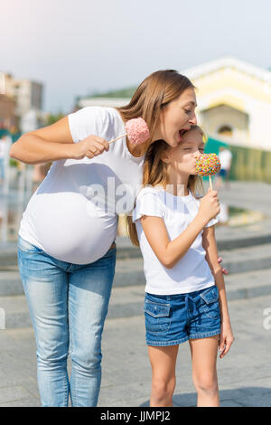 Jolie petite fille et sa mère enceinte manger pommes à la juste dans le parc d'attractions. Heureux famille aimante. Mère et fille s'amuser ensemble. Banque D'Images