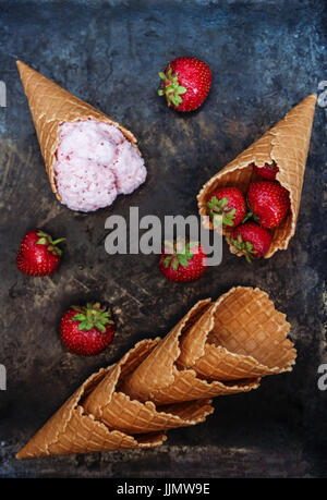 Cornet gaufré avec glace à la fraise, une cuillère de crème glacée et de baies fraîches sur un fond sombre. Banque D'Images