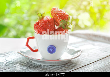 Ripe, rouge, grosses fraises en blanc tasse décoratifs avec stylo rouge sur un arrière-plan flou. Banque D'Images