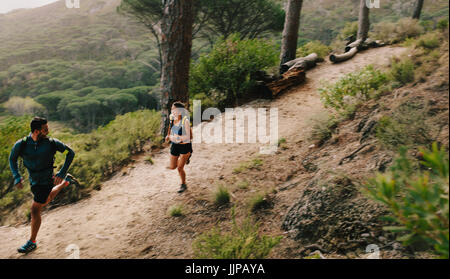 Jeune homme et femme de la formation sur des sentiers de montagne. Couple de mettre en place les athlètes s'exécutant sur sentier de montagne. Banque D'Images