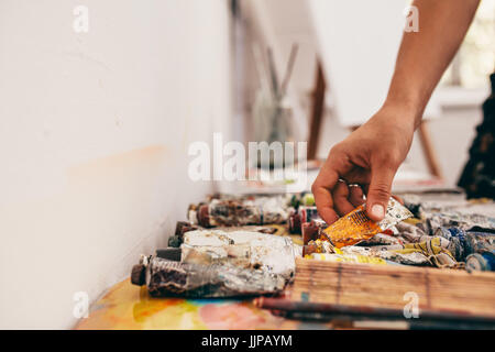 Cropped shot of female artist part ramasser des tubes de couleur de la table. Femme peintre travaillant dans son atelier. Banque D'Images