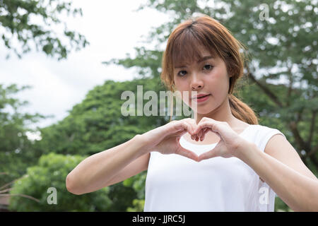 Jeune femme faisant un geste du coeur avec ses doigts. belle fille asiatique montrant son amour avec signe la main dans le parc Banque D'Images