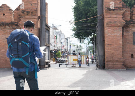 Chiang Mai, Thaïlande - 29 juin 2017 : young asian man wearing blue jeans et blouson reading map debout près de l'ancien mur de briques orange sac avec Banque D'Images