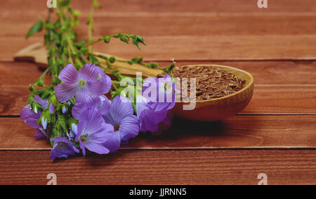 Fleur violette, de lin et de graines dans une cuillère en bois sur un vieux millésime brown table. L'alimentation saine et de suppléments nutritionnels. Soft focus Banque D'Images