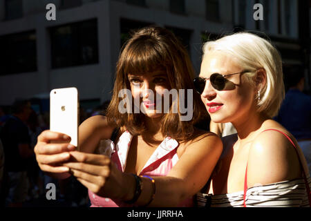 Selfies Smartphone, deux jeunes femmes à la mode d'été vintage prendre un autoportrait, Soho Londres UK London mode rétro. L'appareil photo du smartphone millénaire Banque D'Images
