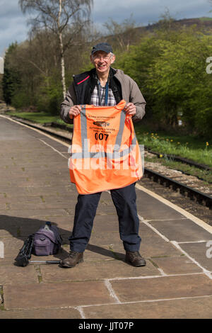 Smiling homme debout sur la plate-forme, posant & holding hi-vis jacket avant l'arrivée de Flying Scotsman - Keighley & Worth Valley Railway, FR, UK. Banque D'Images