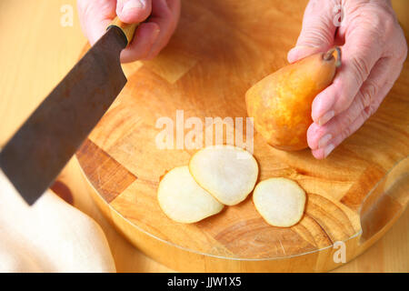 Un homme coupe une poire fraîche en fines tranches sur une planche à découper en bois Banque D'Images