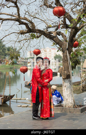 Un jeune couple pose pour des photos de mariage en costume traditionnel que leur page boy nerveusement, et regarde sur à la rivière Banque D'Images