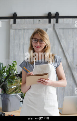 Jeune femme portant des lunettes fleuriste détient portable dans store Banque D'Images