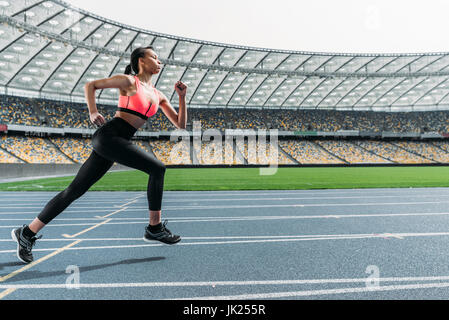 Vue latérale d'athletic young woman in sportswear sprint sur une piste de course stadium Banque D'Images