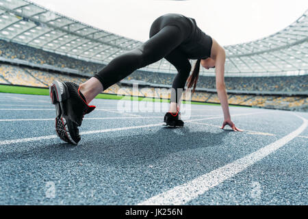 Athletic young woman in sportswear en position de départ sur une piste de course stadium Banque D'Images