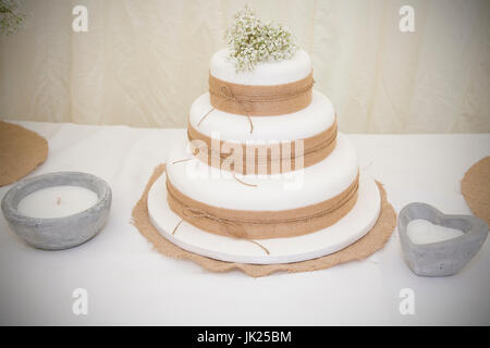 Gâteau de mariage blanc simple avec tissu jute décor et une respiration du bébé blanc arrangement floral.