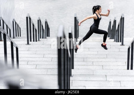 Vue latérale d'athletic young woman in sportswear fonctionnant sur les escaliers du stade Banque D'Images