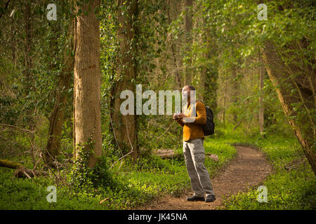 African American man standing on path in forest holding binoculars Banque D'Images