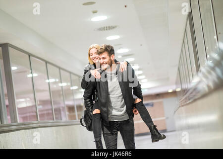 Caucasian man carrying woman piggyback in corridor Banque D'Images