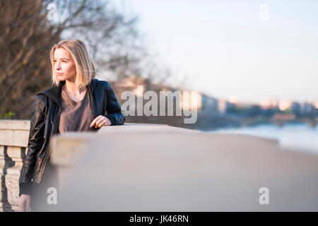 Young woman leaning on wall près de river Banque D'Images