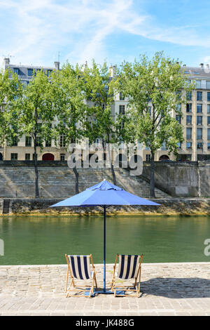 Rayé bleu et blanc deux chaises longues sous un parasol bleu sur la rive de la Seine avec arbres et immeubles parisiens typiques dans le bac Banque D'Images