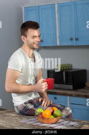 Homme assis sur table en pyjamas, holding red cup. Banque D'Images