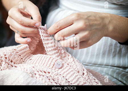 Close-up jeune femme brune avec une queue de cochon avec une profonde coupure sur le chandail coud un bouton avec une aiguille sur un chandail tricoté main rose Banque D'Images
