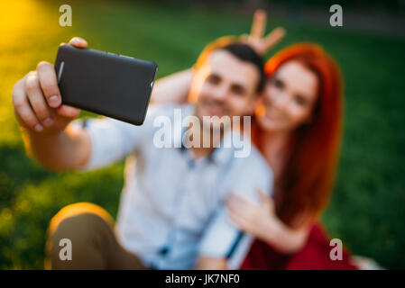 Love couple fait sur téléphone appareil selfies en parc d'été sur le coucher du soleil. Date romantique de jolie femme et jeune homme Banque D'Images