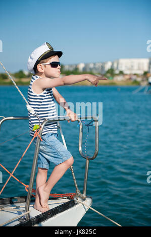 Le capitaine Le capitaine drôle enfant portant chapeau et des lunettes de soleil points la direction avec son doigt debout à bord le bateau yacht Banque D'Images