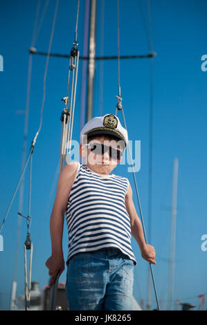 Cool beau petit enfant le capitaine à bord de bateau yacht sur fond de ciel bleu Banque D'Images