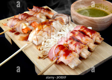 Rouleau avec bacon grillé aux champignons enoki avec du sel et de la sauce dans le style japonais situé sur la plaque en bois. Banque D'Images