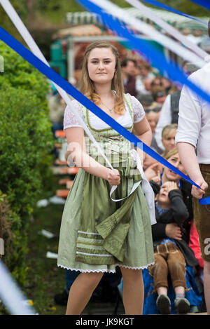 Jeune femme bavaroise traditionnelle en dirndl dress holding ruban blanc lors de l'exécution de la danse folklorique a Bandltanz autour du maypole Banque D'Images