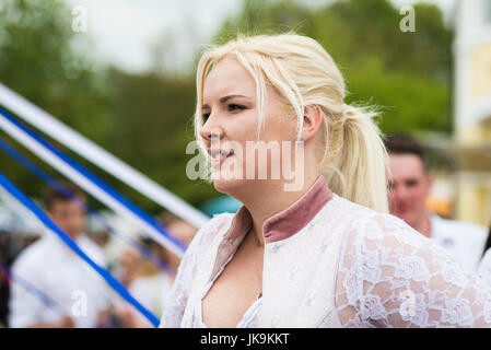 Young woman smiling en dansant une danse folklorique bavarois traditionnel autour d'un mât portant robe dirndl traditionnel Banque D'Images