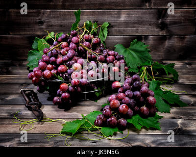 Les raisins rouges frais bouquet allongé sur feuilles sur une vieille table en bois. Banque D'Images
